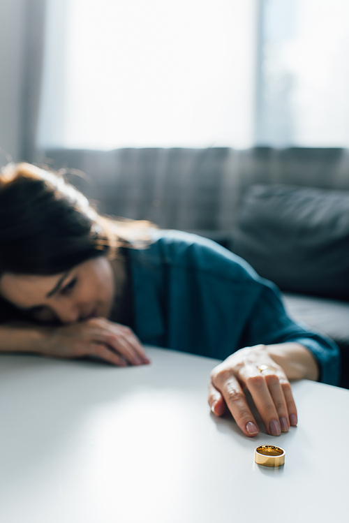 selective focus of depressed woman reaching golden ring on coffee table, divorce concept