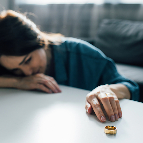 selective focus of sad woman reaching golden ring on coffee table, divorce concept