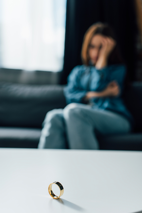 selective focus of golden ring on coffee table near sad woman, divorce concept