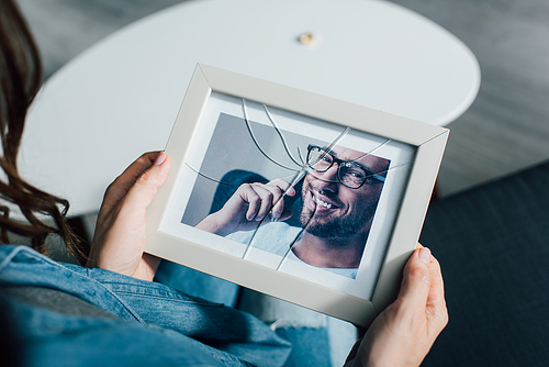 cropped view of woman holding photo of husband in frame with broken glass, divorce concept