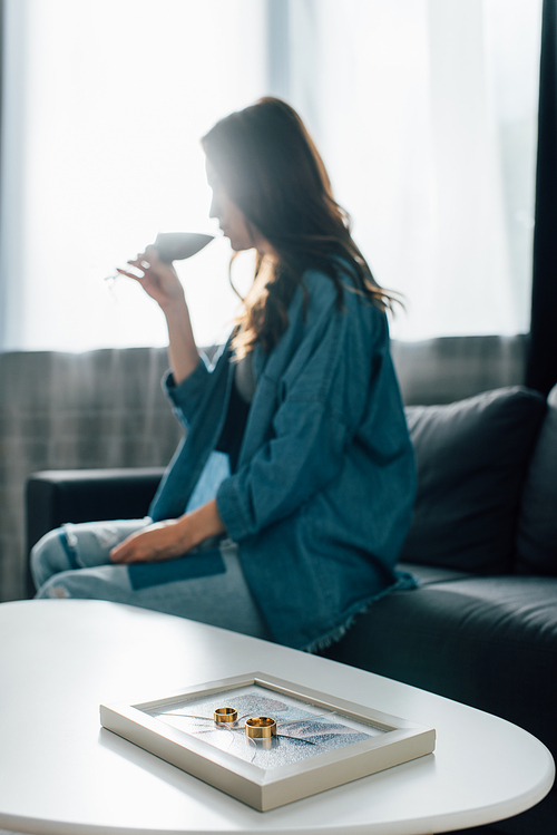 selective focus of golden rings on photo frame with broken glass near woman drinking wine, divorce concept