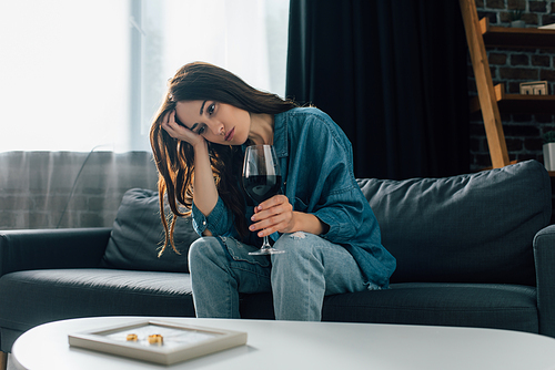selective focus of sad woman with glass of wine near golden rings on photo frame, divorce concept