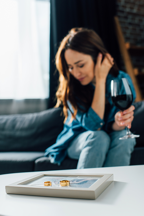 selective focus of golden rings on photo frame near sad woman with glass of wine, divorce concept