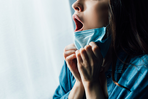 partial view of scared woman with open mouth touching medical mask