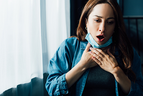 scared woman with open mouth in medical mask touching throat