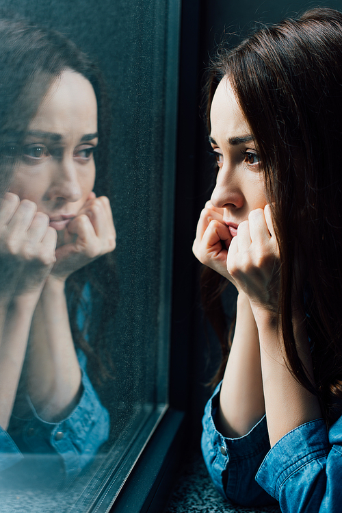 sad brunette woman touching face while looking at window