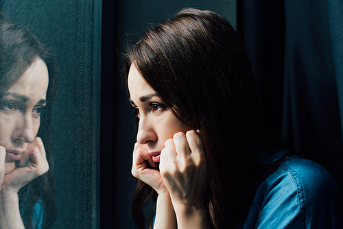depressed brunette woman touching face while looking at window