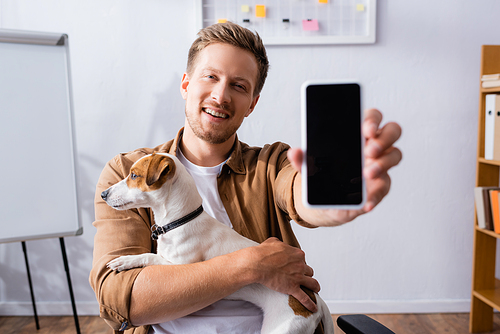 selective focus of businessman showing smartphone with blank screen while holding jack russell terrier dog
