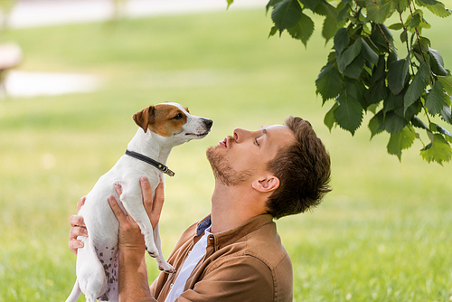 side view of young man holding white jack russell terrier dog with brown spots on head