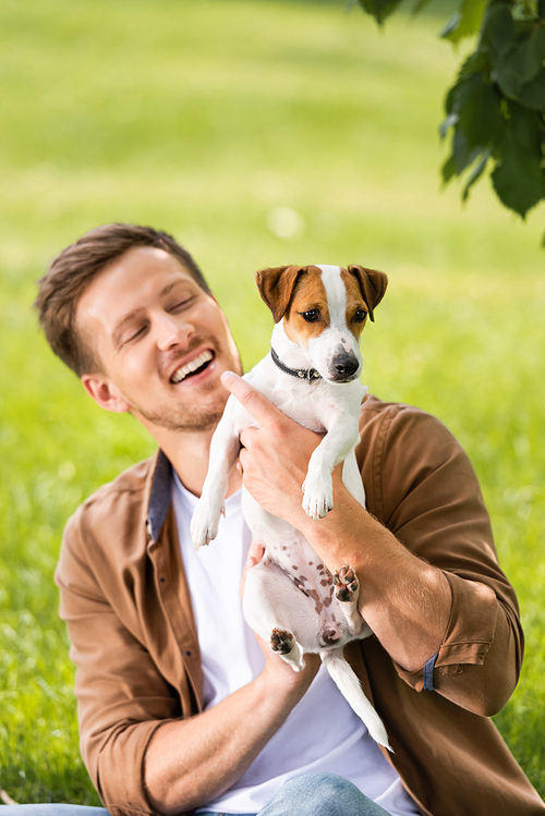young man in brown shirt holding white jack russell terrier dog with spots on head