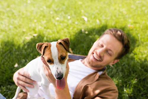 young man holding jack russell terrier dog while relaxing on green grass