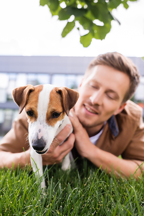 selective focus of young man lying on green grass with jack russell terrier dog