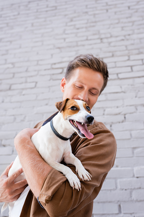 Selective focus of young man holding jack russell terrier near building