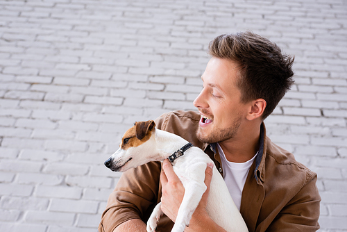 Low angle view of excited man holding jack russell terrier near facade of building