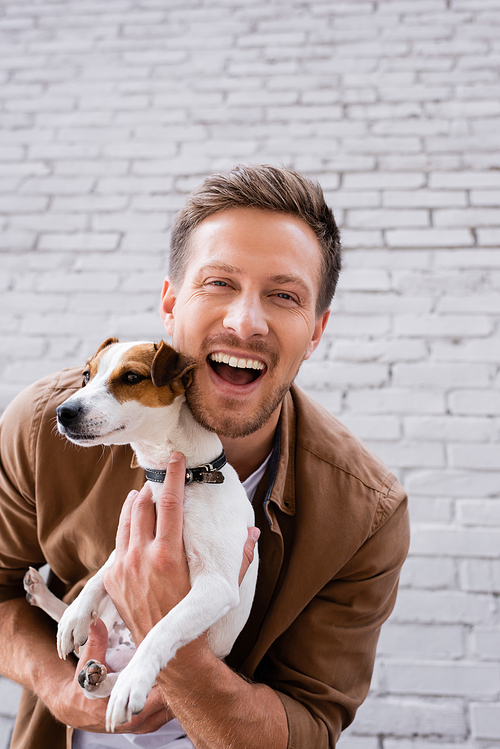 Young man  while embracing jack russell terrier near facade of building