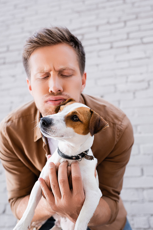 Selective focus of man with face expression embracing jack russell terrier on urban street