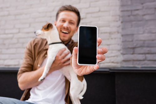 Selective focus of man showing smartphone and holding jack russell terrier on urban street