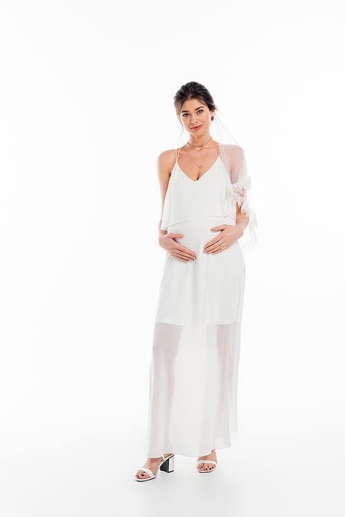 full length view of pregnant bride touching belly while  on white