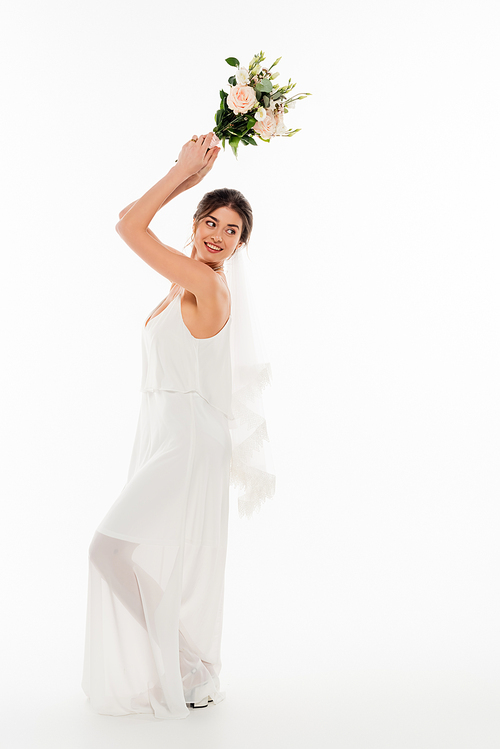 full length view of cheerful bride throwing wedding bouquet on white