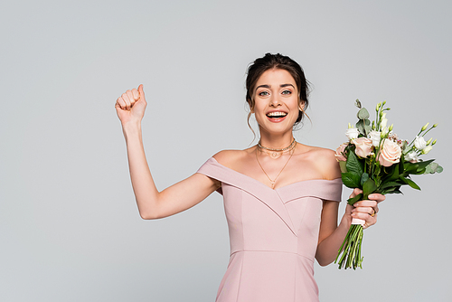 excited fiancee showing win gesture while holding wedding bouquet isolated on grey