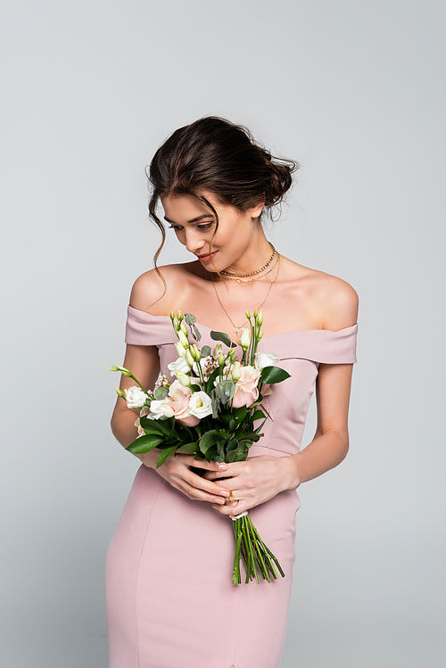 happy young bride in pink dress holding wedding bouquet isolated on grey