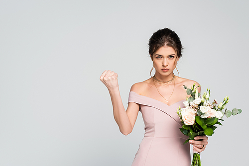 serious woman showing clenched fist while holding wedding bouquet isolated on grey