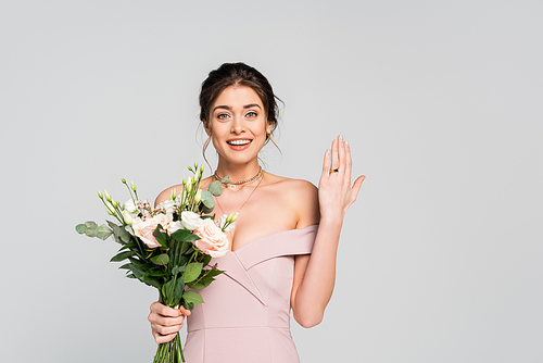 joyful woman showing wedding ring while holding flowers isolated on grey