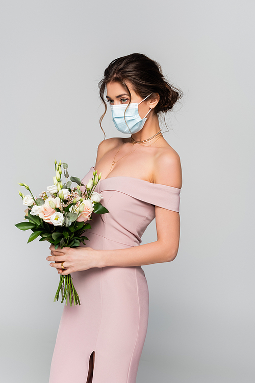 young bride in pink dress and medical mask posing with wedding bouquet isolated on grey