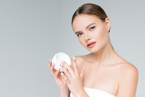 young woman holding container with face cream isolated on grey