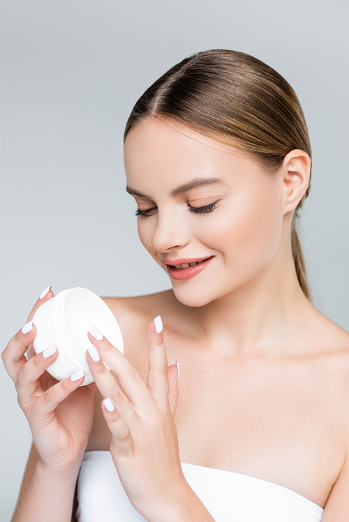 happy young woman holding container with face cream isolated on grey