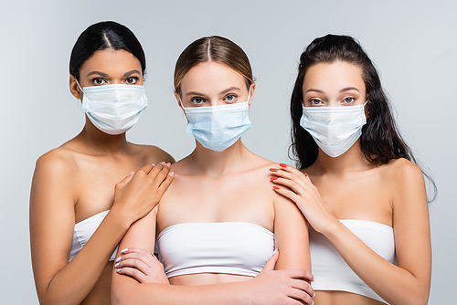 multiethnic women in tops with bare shoulders and medical masks isolated on grey