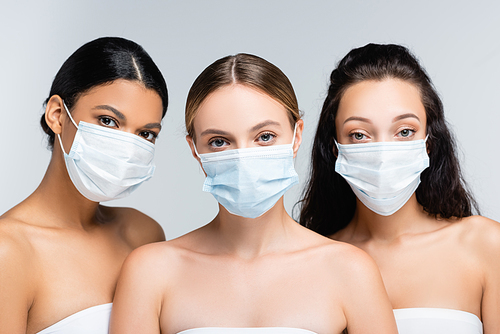 young multiethnic women in tops with bare shoulders and medical masks isolated on grey