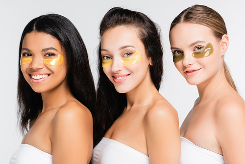 happy multiethnic women with naked shoulders in eye patches smiling isolated on white