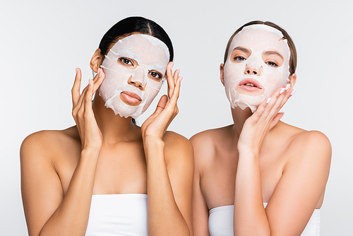 young multiethnic women applying moisturizing sheet masks isolated on white