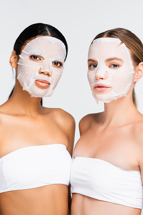 interracial young women in moisturizing sheet masks isolated on white