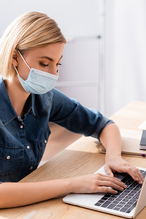 young manager in medical mask typing on laptop in office