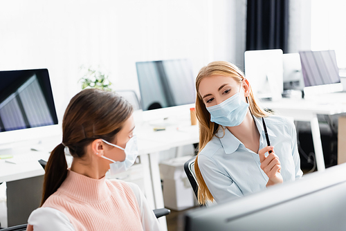 Businesswomen in medical masks talking near computer in office