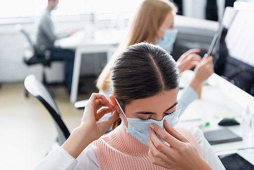 Businesswoman wearing medical mask while colleagues working on blurred background in office
