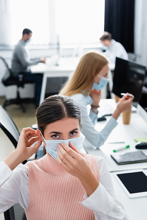 Businesswoman  while wearing medical mask near colleague on blurred background