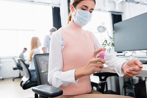Businesswoman in medical mask using hand sanitizer in office
