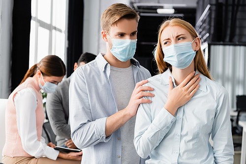 Businessman in medical mask standing near ill colleague in office