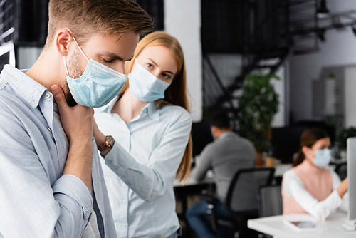 Ill businessman in medical mask touching neck near colleague on blurred background
