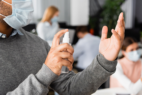Cropped view of indian businessman in medical mask using hand sanitizer in office