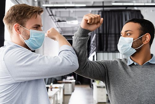 Multiethnic businessmen in medical masks giving high five with elbows