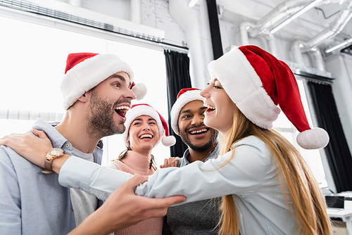 Smiling multiethnic businesspeople embracing while celebrating christmas in office
