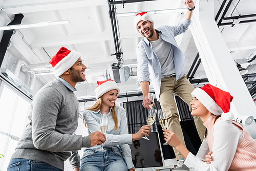 Multiethnic businesspeople with glasses of champagne and santa hat celebrating Christmas in office