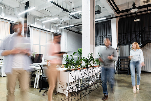 Motion blur of businesspeople walking near computers and plants in office
