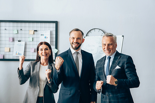 Cheerful businesspeople showing yeah gesture near flipchart in office