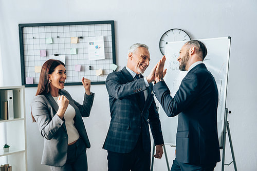 Smiling businessman giving high five near cheerful businesswoman in office