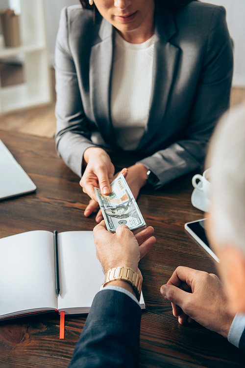 Investor giving dollars to businesswoman on blurred background in office